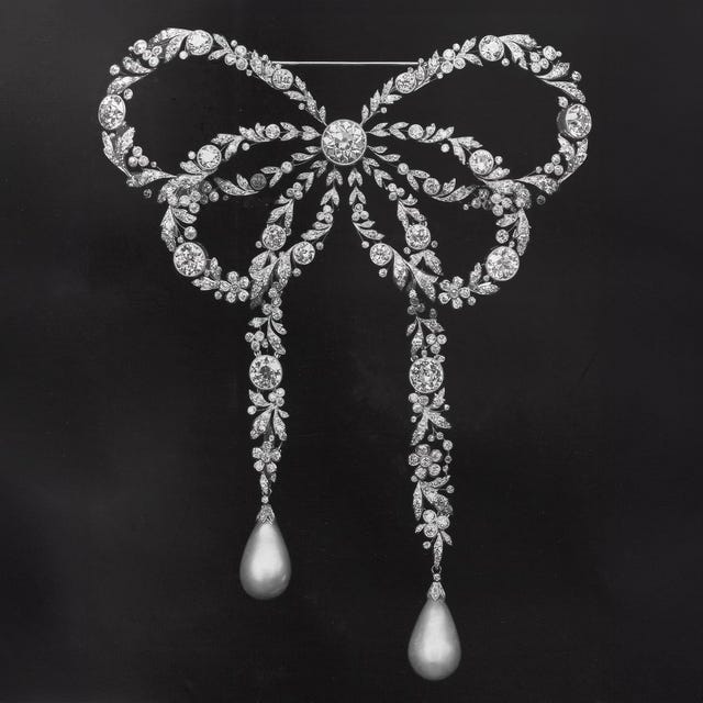 Elegant diamond brooch shaped like a bow with pearl accents, showcased against a dark background.
