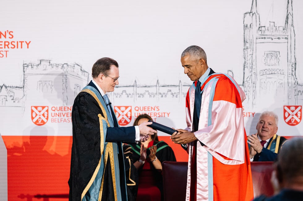 Two figures in academic regalia exchanging a diploma during a ceremony at Queen's University Belfast.