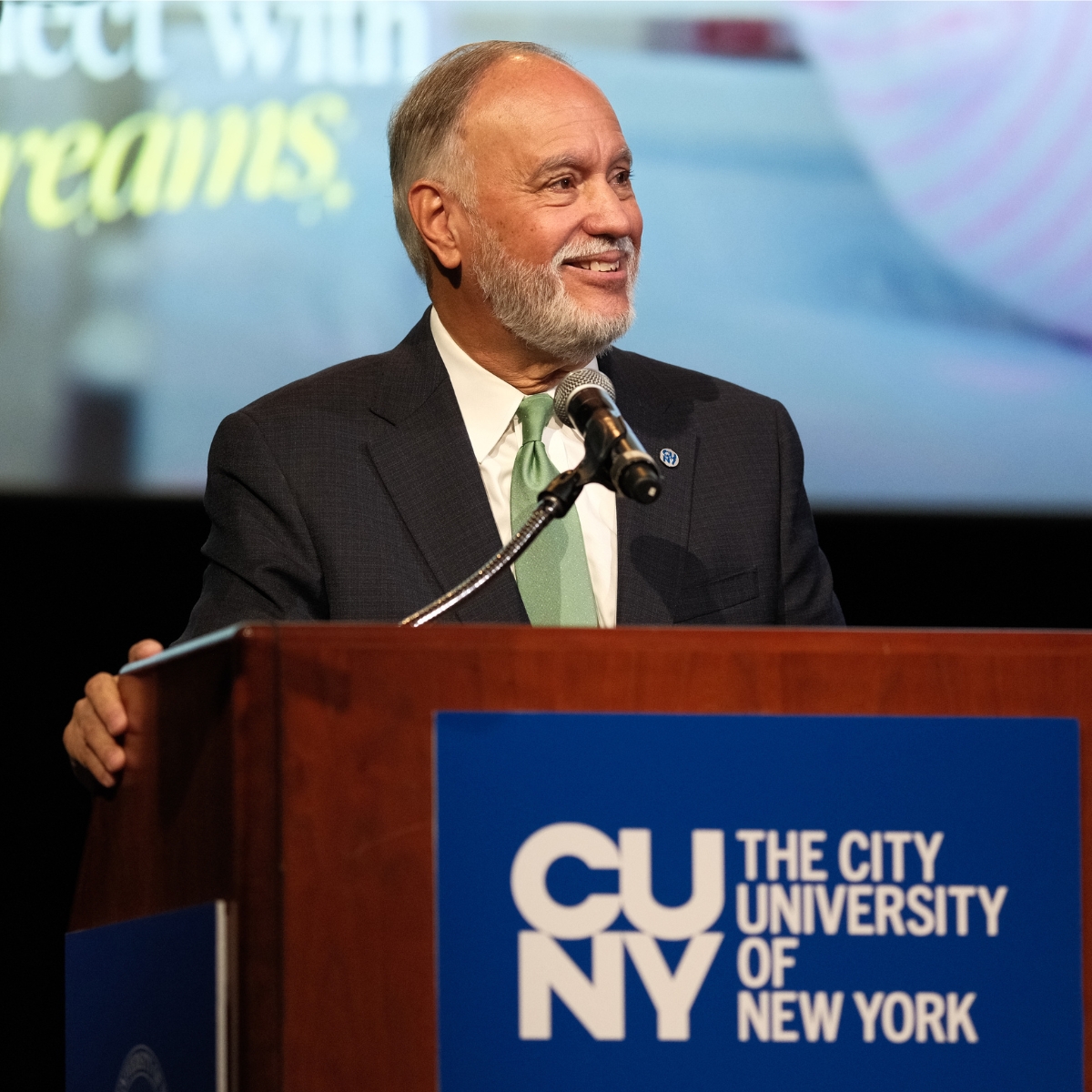 Man in suit speaks at podium with CUNY logo