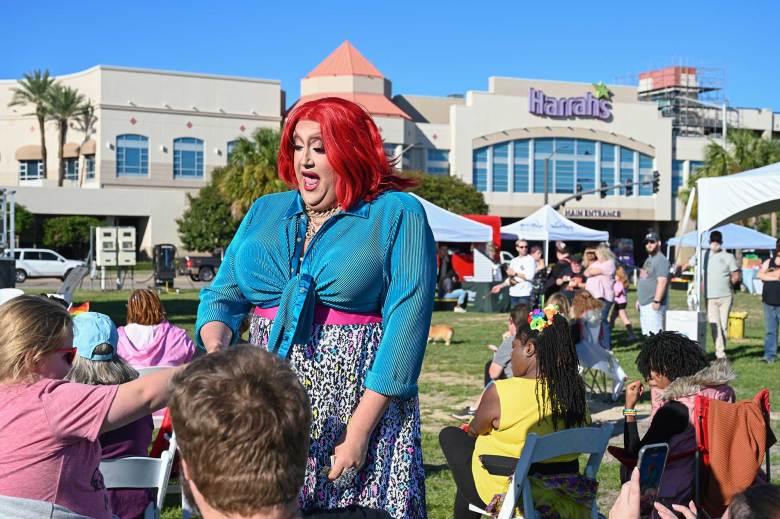 A drag queen with bright red hair and a blue and leopard print dress performs at a festival held outside