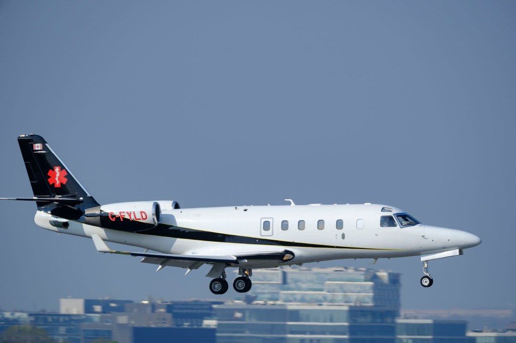 A white and black medevac airplane with landing gear deployed, in flight against a clear sky.
