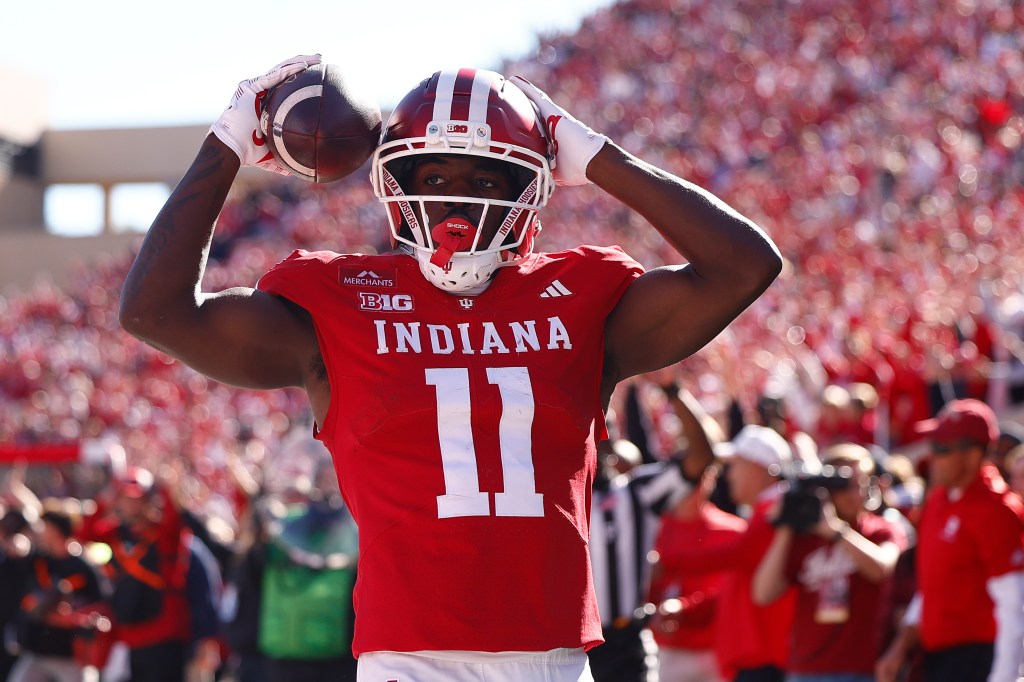 An Indiana football player holding a football above his head in front of a stadium crowd.