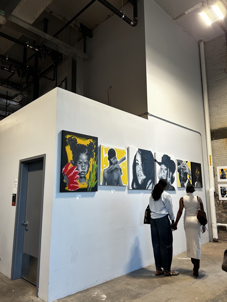 Attendees view a display of portrait paintings at CultureCon 2026 at the Brooklyn Navy Yard in Brooklyn, New York. Photo by Catherine Roth / The Haitian Times
