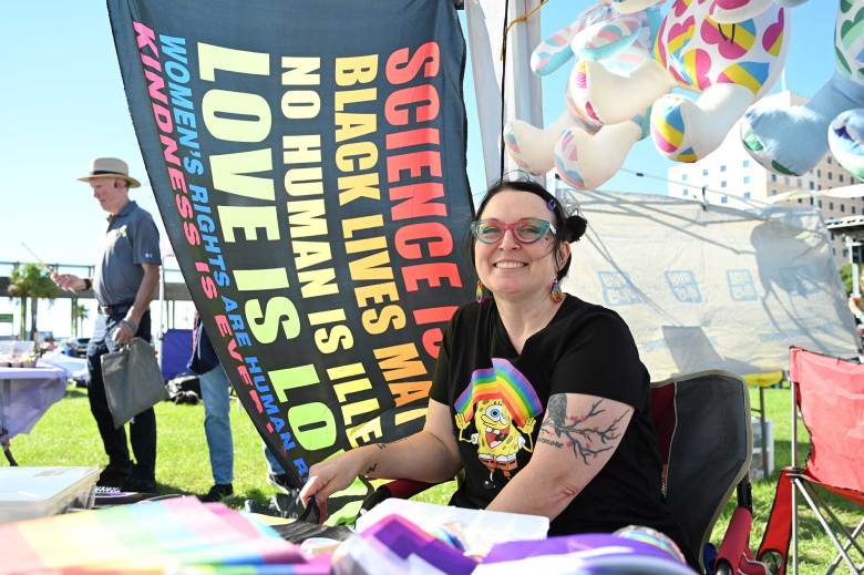 someone wearing pride merch sits in front of a rainbow flag