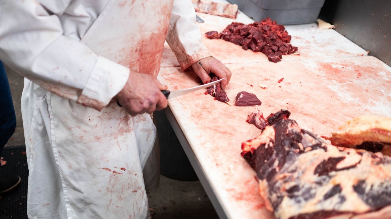 A butcher cutting beef on a white table.