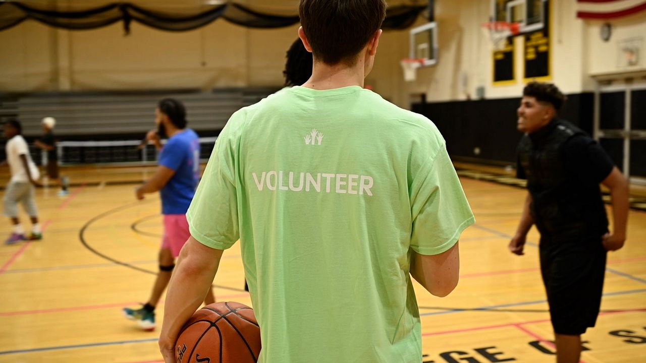 Volunteer works with students on a basketball court for YMCA programming.