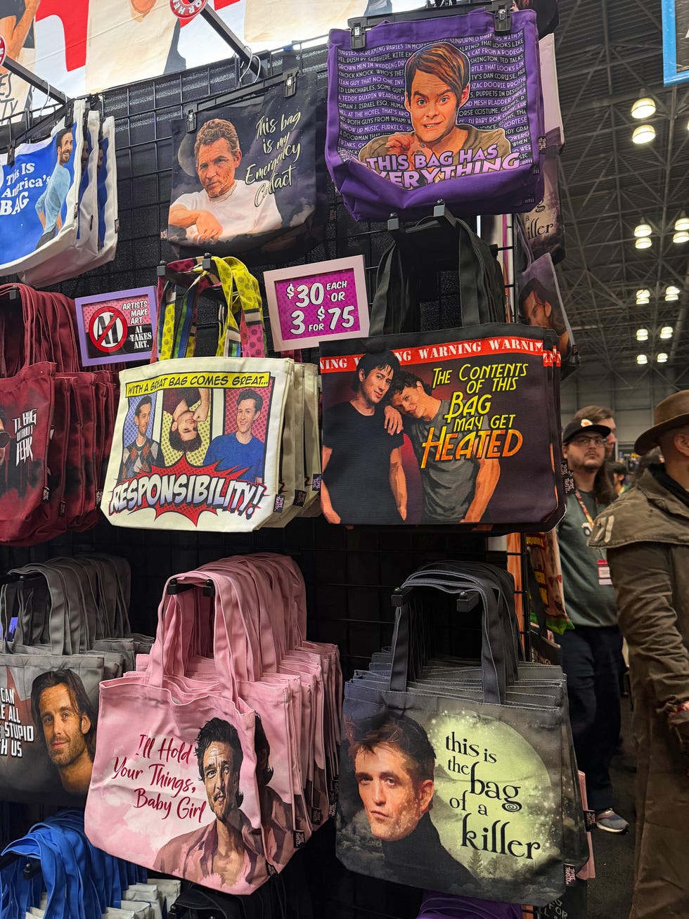 Tote bags hanging in a display featuring humorous and dramatic phrases and images of various characters or personalities. Tote bags hanging in a display featuring humorous and dramatic phrases and images of various characters or personalities.