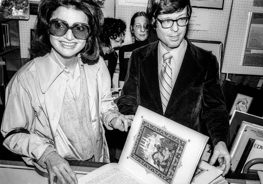 Jacqueline Kennedy Onassis (1929 - 1994) (left) and Gotham Book Mart owner Andreas Brown (1933 - 2020) as they pose with an unpublished copy of the Russian folk tale 'The Firebird' at the International Antiquarian Book Fair at the Plaza Hotel, New York, New York, April 1, 1977. Onassis later edited a new version of the folk tale