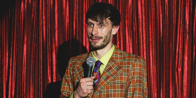 Donny on stage holding a microphone in front of a red curtain in Netflix's Baby Reindeer. 