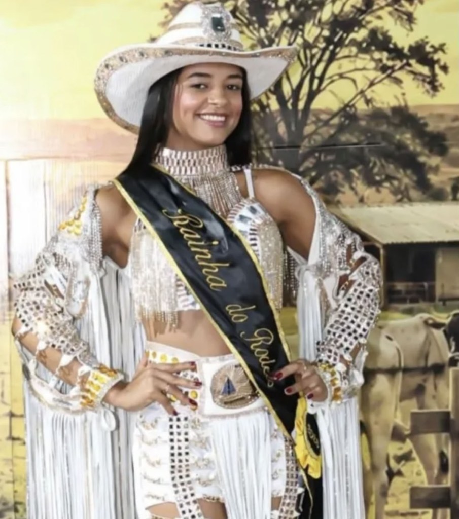 Ana Beatriz Araújo Ferreira wearing a white rodeo outfit, a cowboy hat, and a sash reading "Rainha do Rodeio".