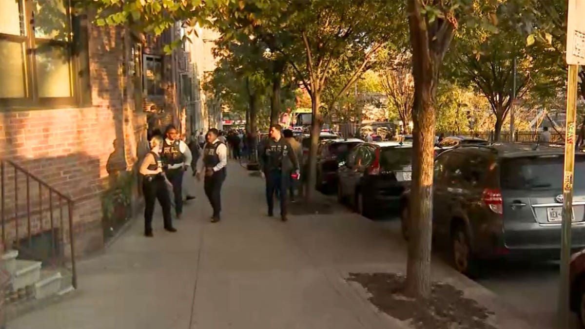 Law enforcement personnel walk along a sidewalk near the scene of a shooting in the Bronx