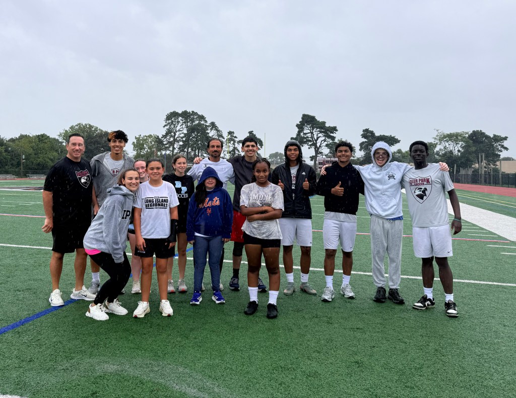 Coach Frank Vertullo poses with soccer players on a field in Deer Park.
