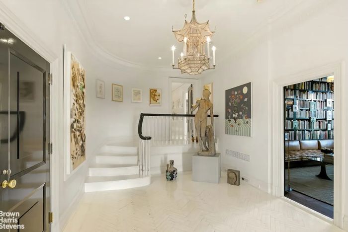 A listing photo shows a Tony Matelli sculpture at the end of a long entryway that leads up to the apart. The doors to the right open to another bedroom, currently furnished as a library.