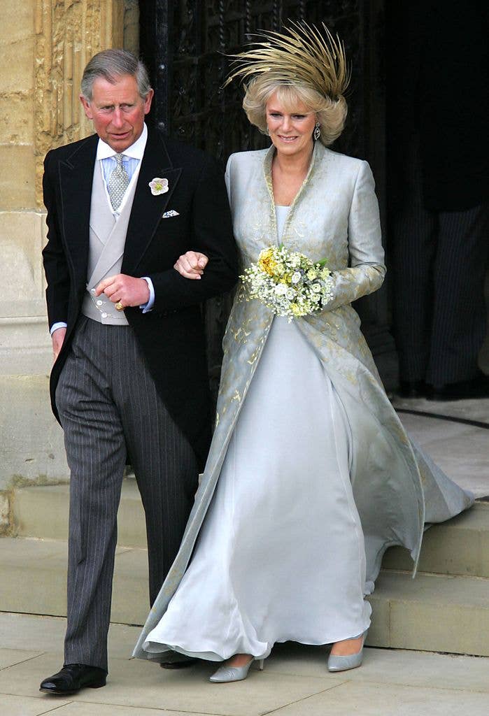 King Charles in a black suit and his wife in a silver gown, holding hands on steps.