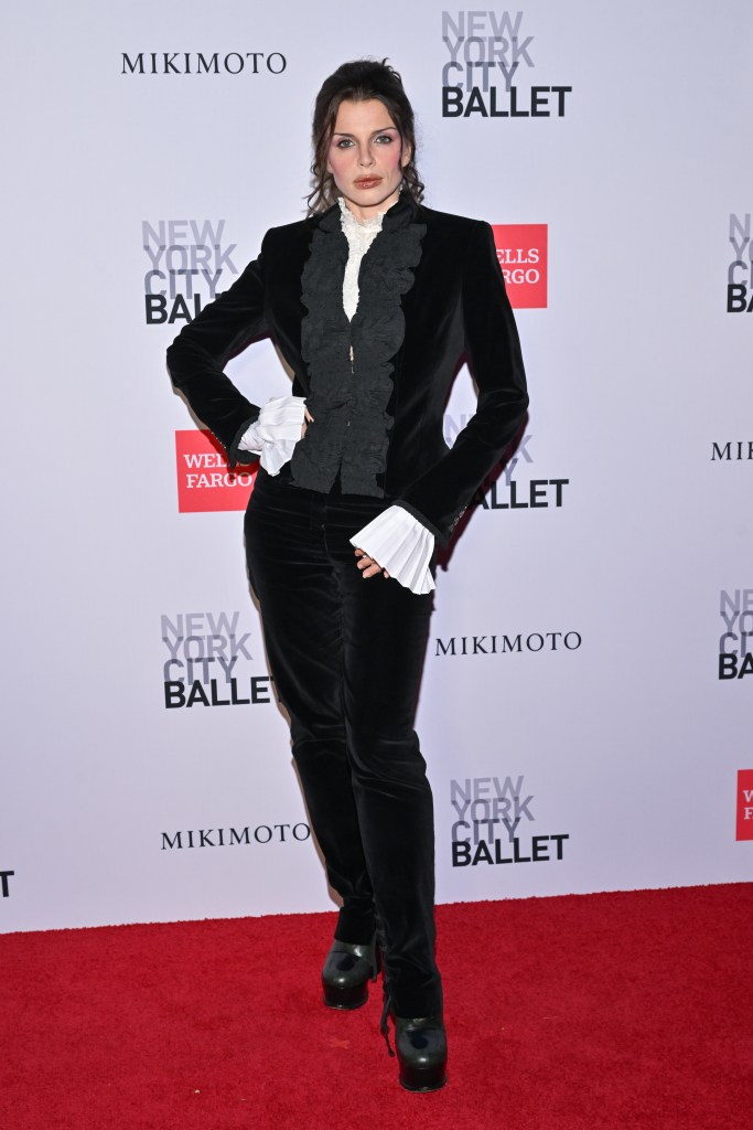 Julia Fox wearing a black velvet suit with ruffled cuffs and collar on a red carpet.