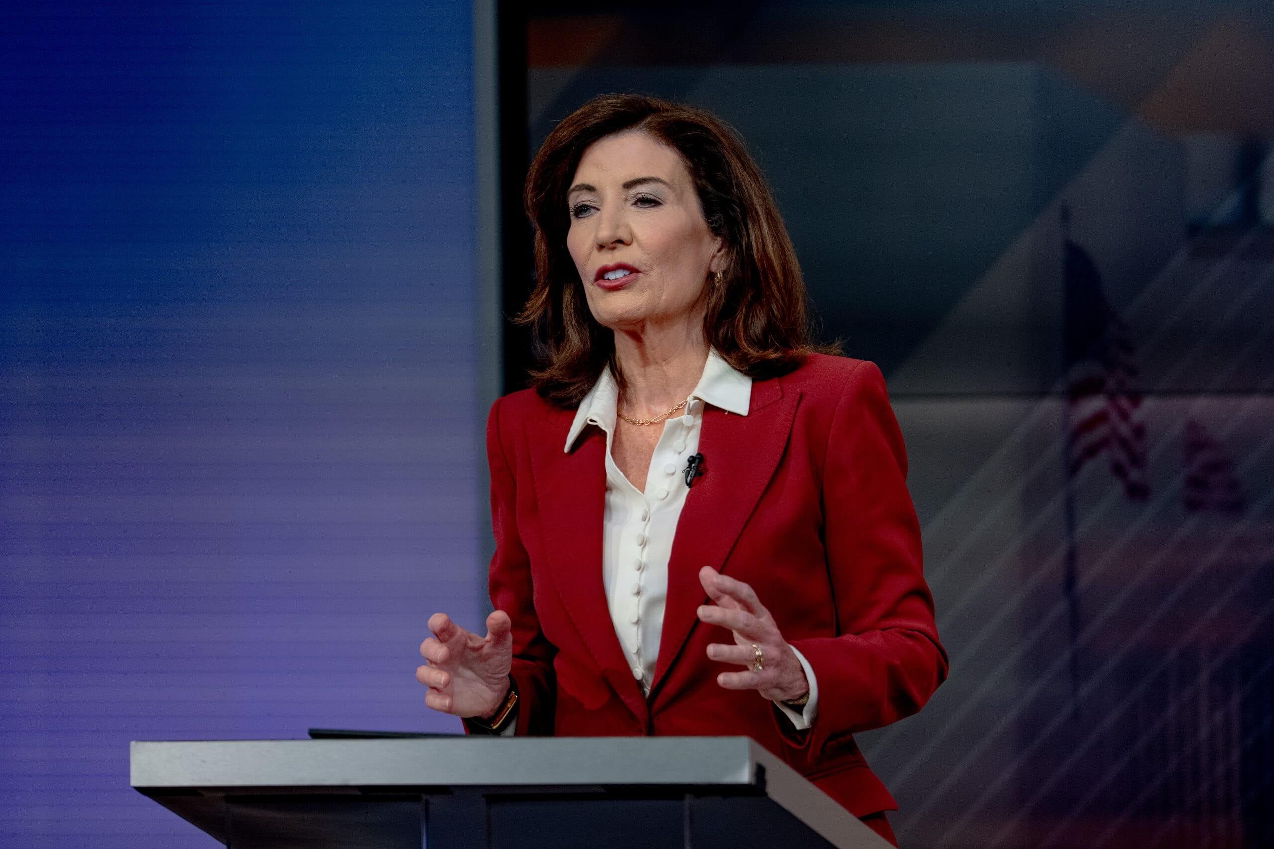 Gov. Hochul at a podium wearing a red blazer