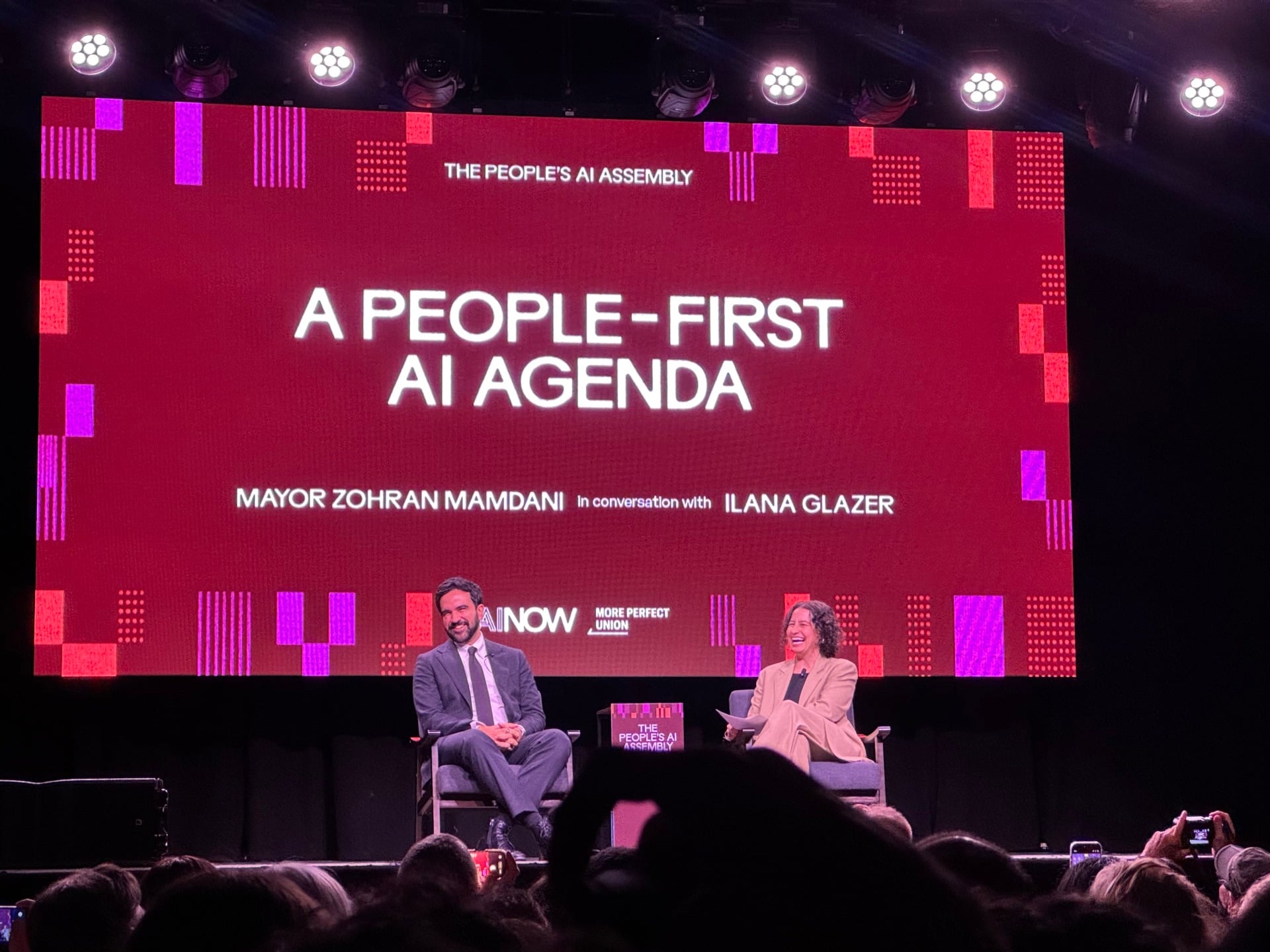 Mayor Zohran Mamdani and actress Ilana Glazer on stage in front of a screen that reads "A People-First AI Agenda"