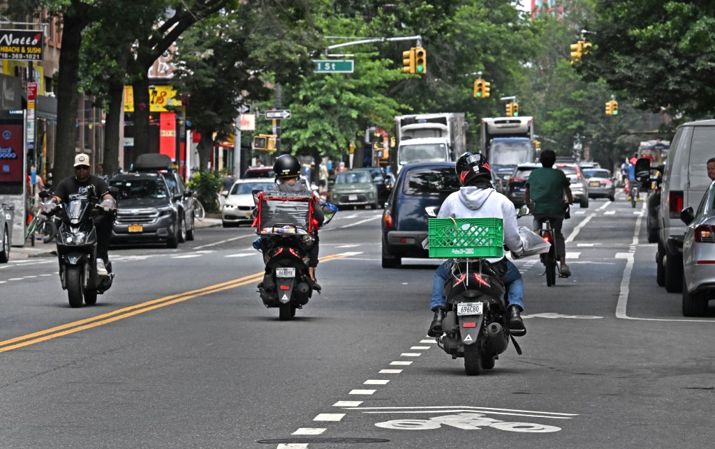 Mopeds and e-bikes ride along a New York City street with traffic.