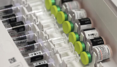 Rows of single-dose vials with green caps lined up beside prefilled diluent syringes in a storage tray.