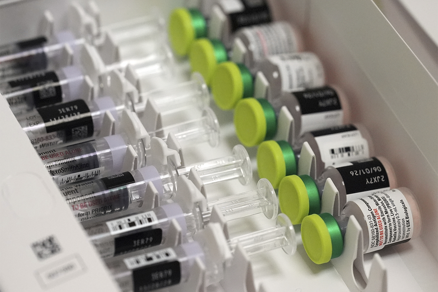 Rows of single-dose vials with green caps lined up beside prefilled diluent syringes in a storage tray.
