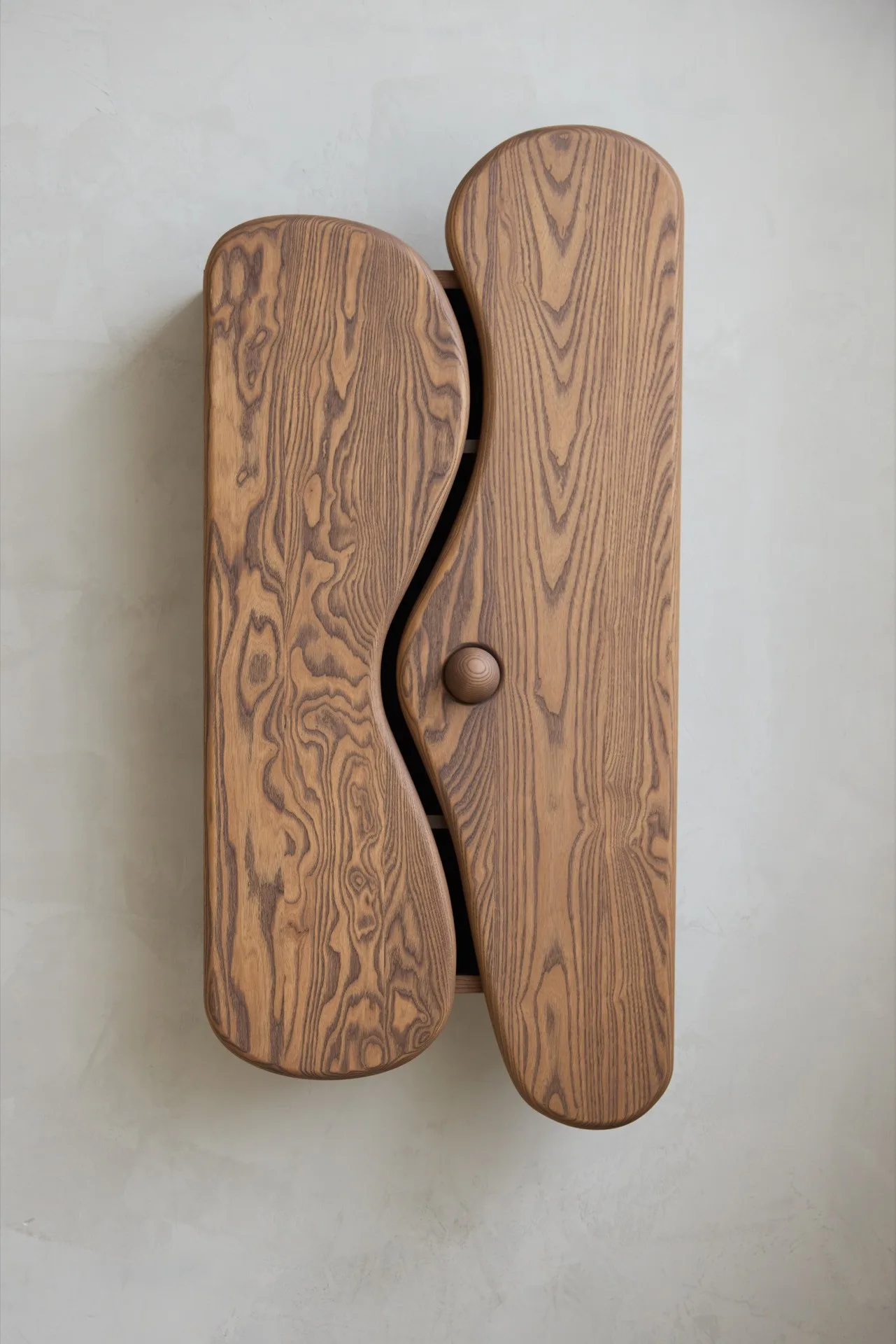 Wall-mounted wooden cabinet with two curved doors and a round knob, showing wood grain.
