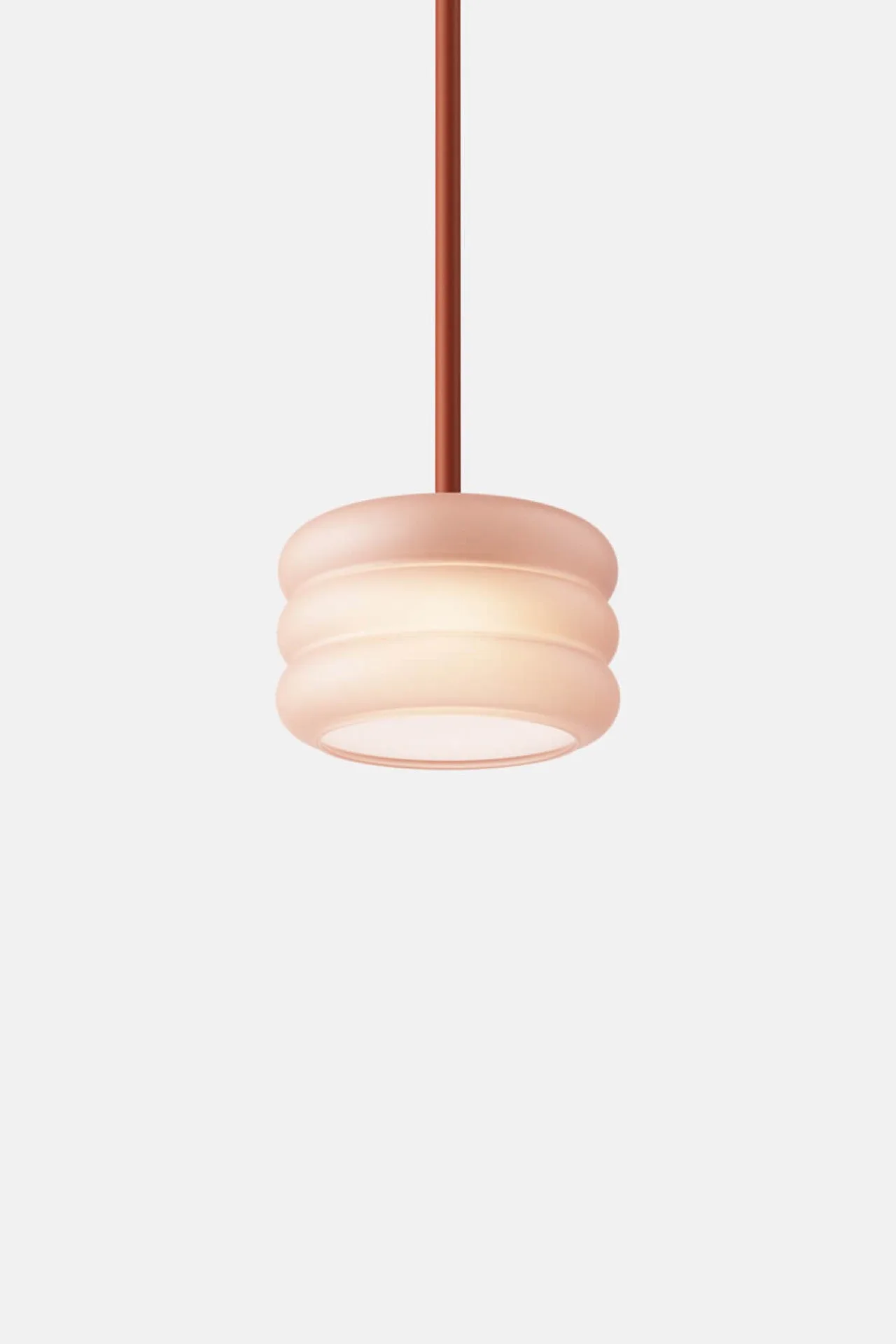 Round, pink pendant light with ribbed design hanging from a thin rod on white.