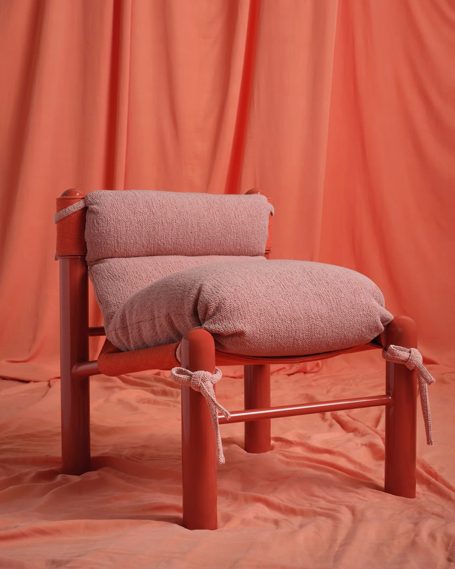 Modern chair with plush pink cushion and red frame on draped red fabric backdrop.