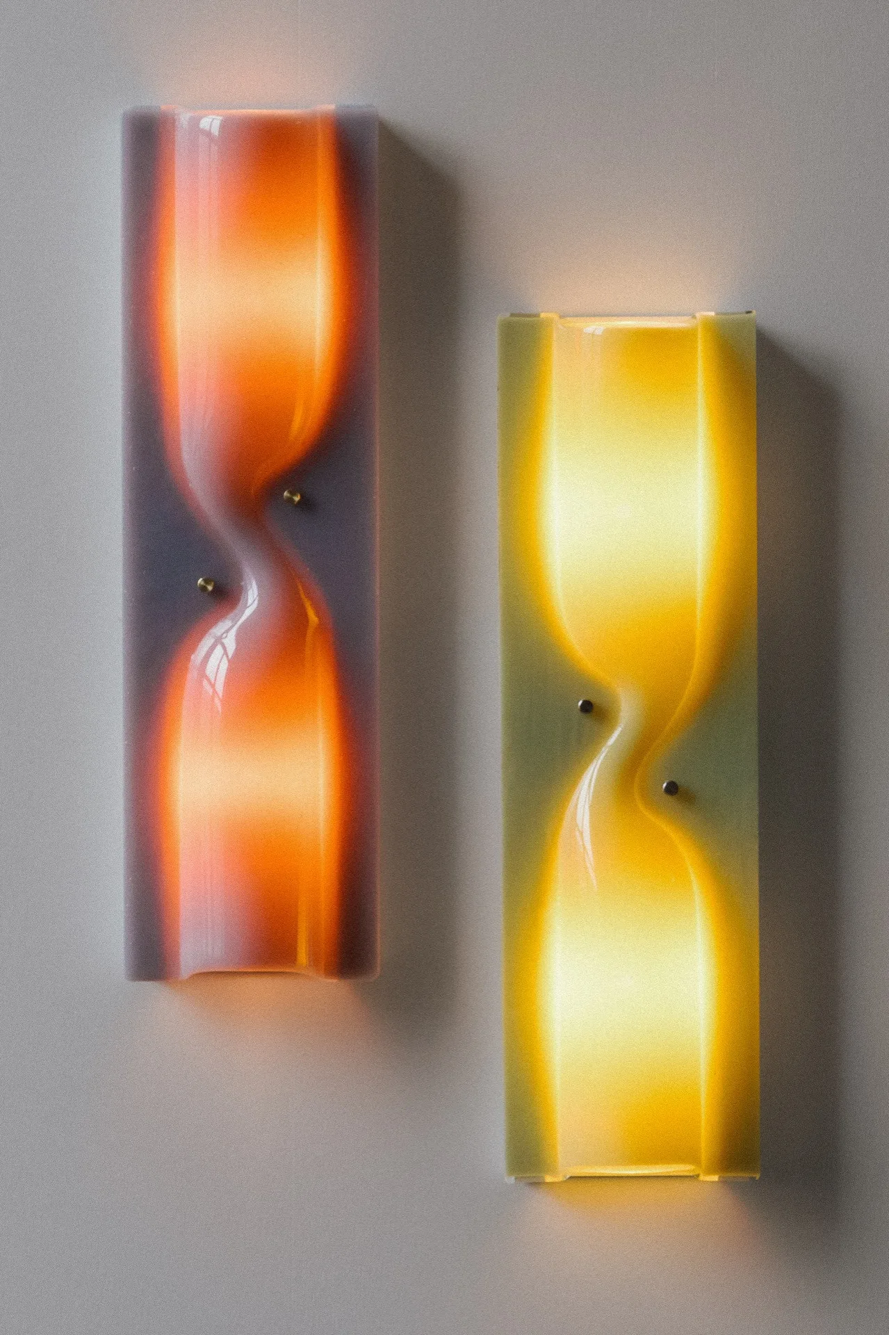Two rectangular wall sconces with hourglass designs emitting warm orange and yellow light.