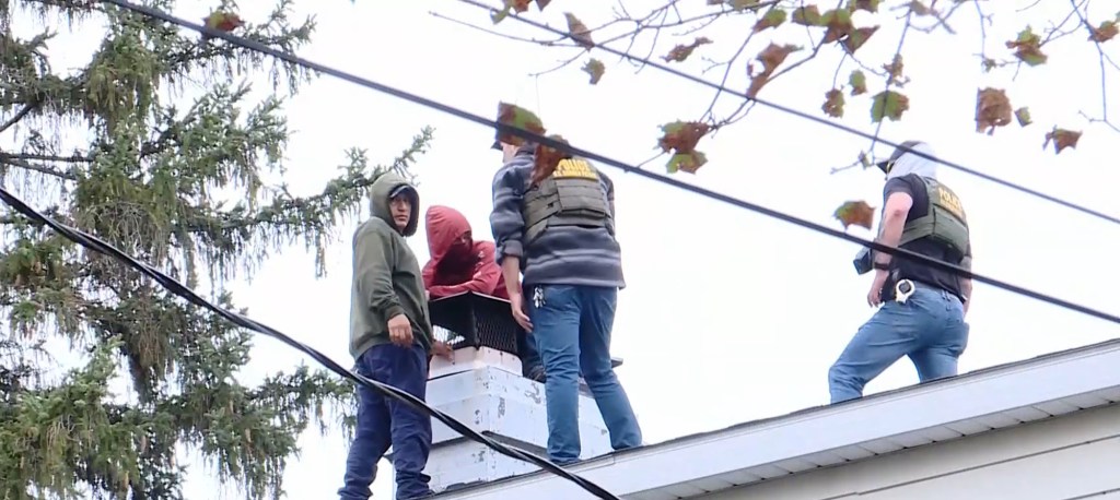 Two men stand on a roof next to police officers during a standoff in Oswego, New York.