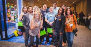 Group of Small Business Expo attendees wearing event badges and holding green tote bags on the exhibit floor.