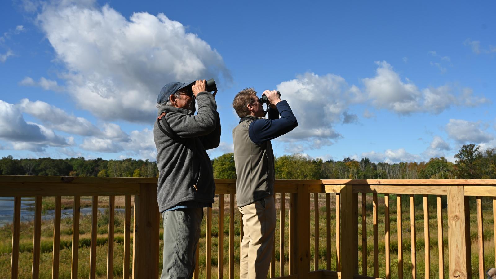 Two people on raised platform looking out onto scenic land with binoculars