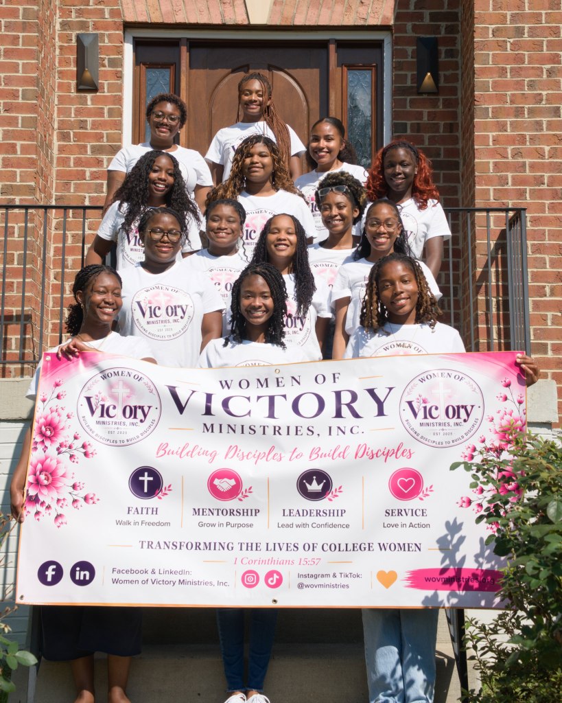 Photo of members of Women of Victory Ministries holding a banner in front of a brick building.