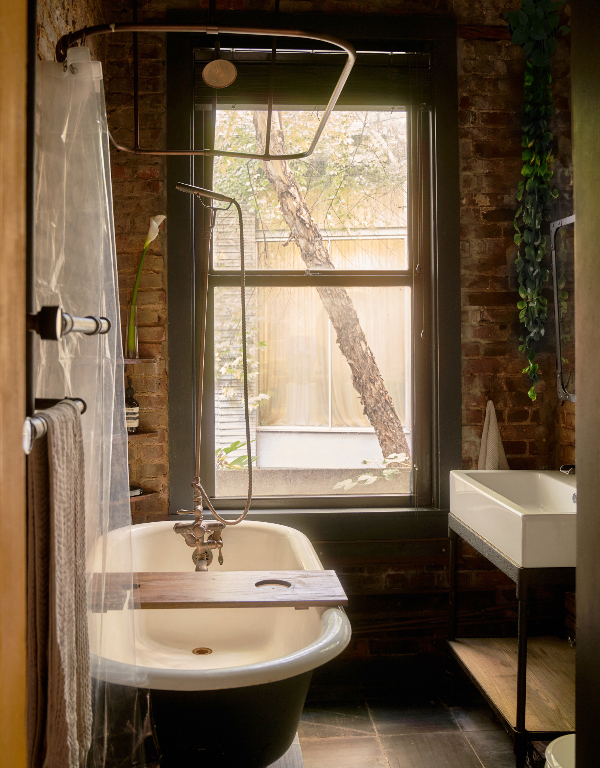 An NYC loft small bathroom with a shower over a free-standing tub by a white sink with a storage shelf below