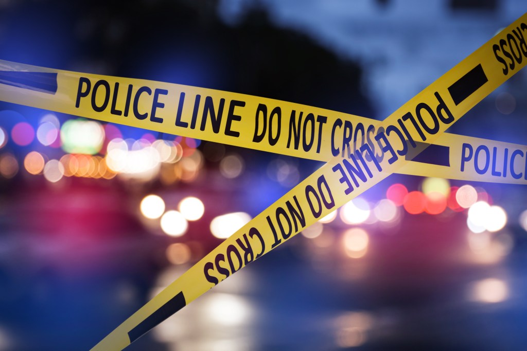 Yellow law enforcement tape isolating a crime scene with a blurred city street in the background.