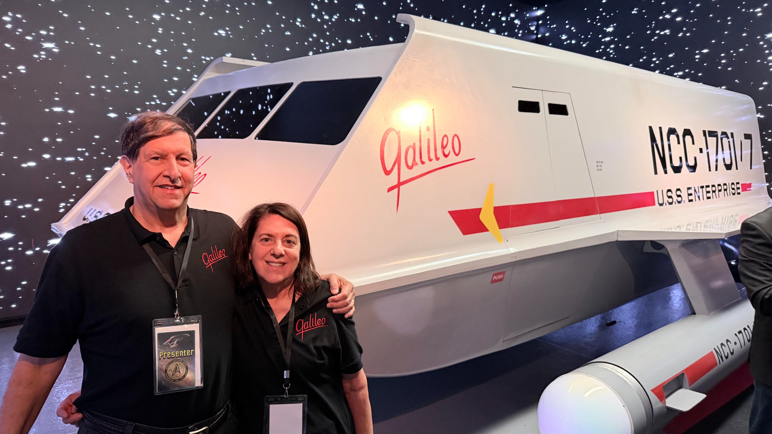 a man and his wife standing before a sci-fi shuttle mock-up