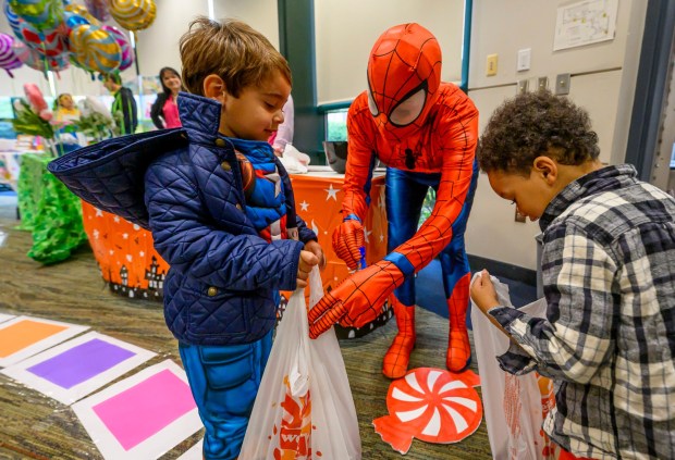 Dressed as Spiderman, Cyndi King, gives candy to Josiah, 4, and Hayden, 3, of Dream Garden Daycare And Learning Center on Friday, Oct. 31, 2025, during a Trick-or-Treat Candy Land themed adventure hosted by Lehigh County at Government Center in Allentown. (April Gamiz/The Morning Call)