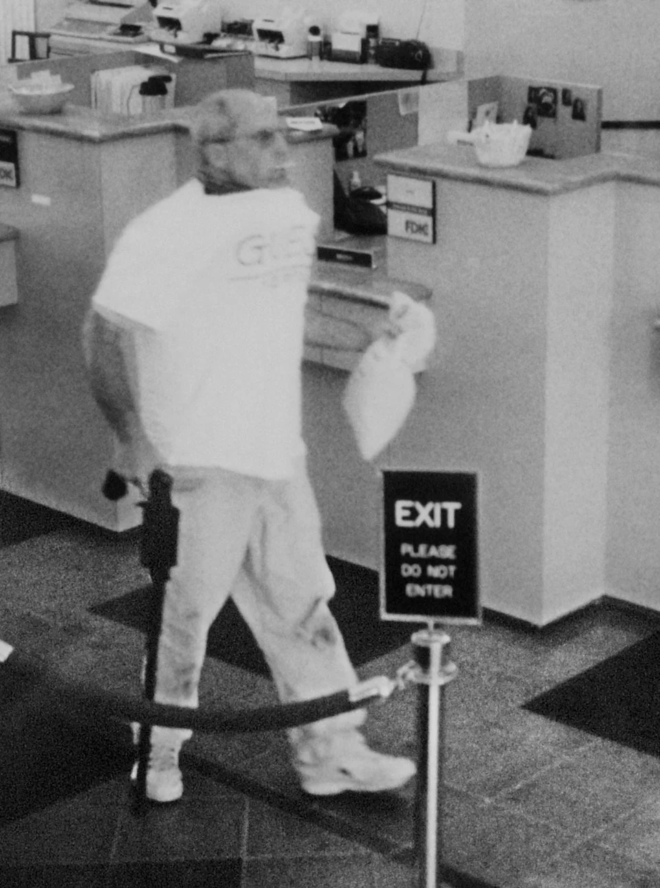 Brian Wells is seen leaving the PNC bank in Summit Towne Centre south of Erie on Aug. 28, 2003. He is carrying a cane gun and wearing a collar bomb, which is protruding from under his shirt. This image was taken after he received money from the teller. In his mouth is a lollipop that he picked up while waiting to approach the teller. Wells later died when the collar bomb detonated.