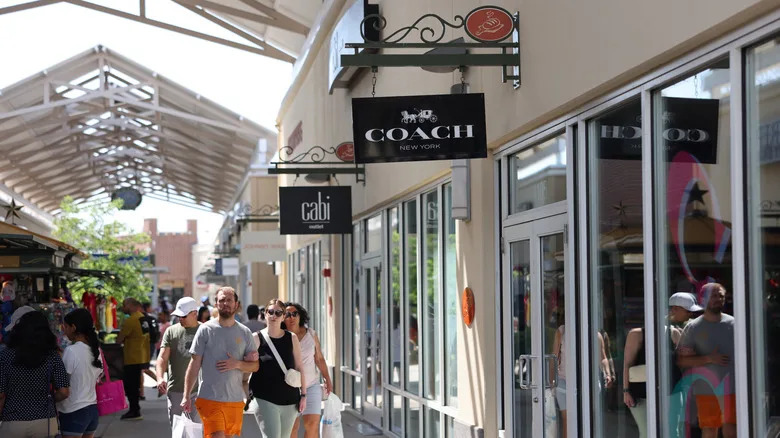 Shoppers walking through the Philadelphia Premium Outlets, with signs for Coach and Cabi along the right side of the walkway