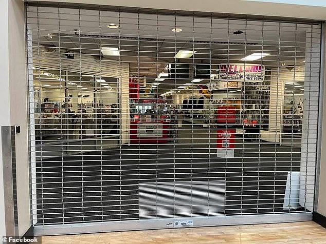 A retail store with all its lights shinning while behind a metal gate as no workers or customers appear to be seen