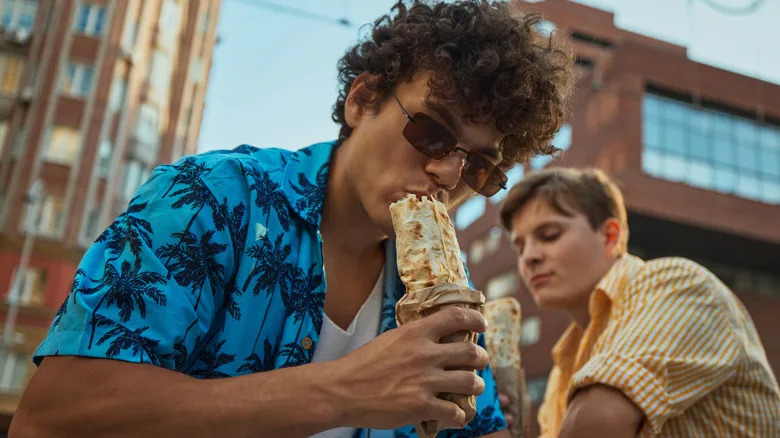 two young men eating burritos in the city