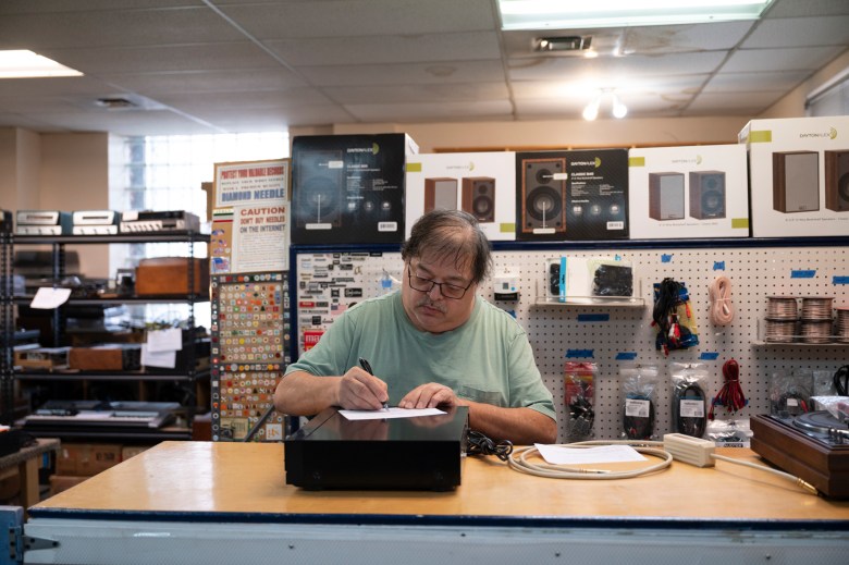 A man with glasses and a mustache labels a recently repaired stereo