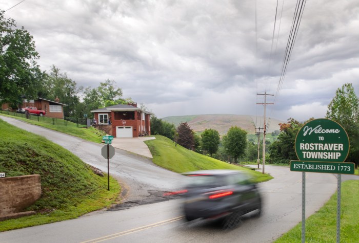 A car on a suburban street with a large mound in the background.