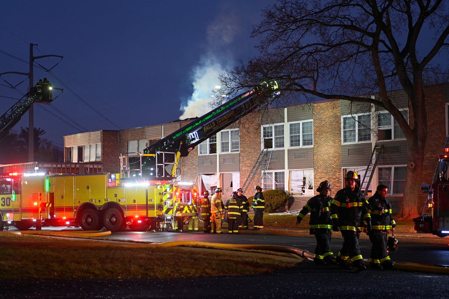 Emergency vehicles and personnel stand outside a burning building.