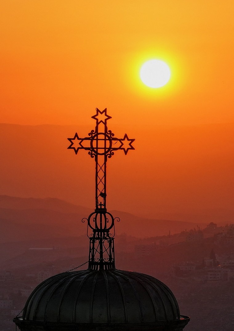 The sun rises in the sky over a cross on top of a building