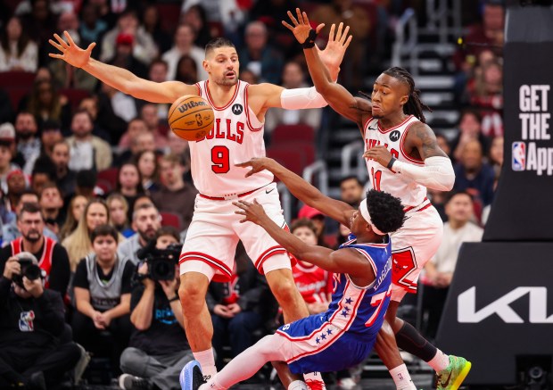 Philadelphia 76ers guard Vj Edgecombe (77) passes the ball while falling as Chicago Bulls center Nikola Vučević (9) and Chicago Bulls guard Ayo Dosunmu (11) try to block it in the second quarter, Friday, Dec. 26, 2025, at the United Center in Chicago. (Dominic Di Palermo/Chicago Tribune)