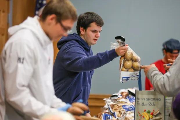 J.J. Grochal, a junior member of the Pittston Area football team, hands out a bag of potatoes during the launch of the Pittston City Food Distribution Pantry at the Pittston Memorial Library on Thursday, Dec. 11, 2025. (JASON ARDAN / STAFF PHOTOGRAPHER)