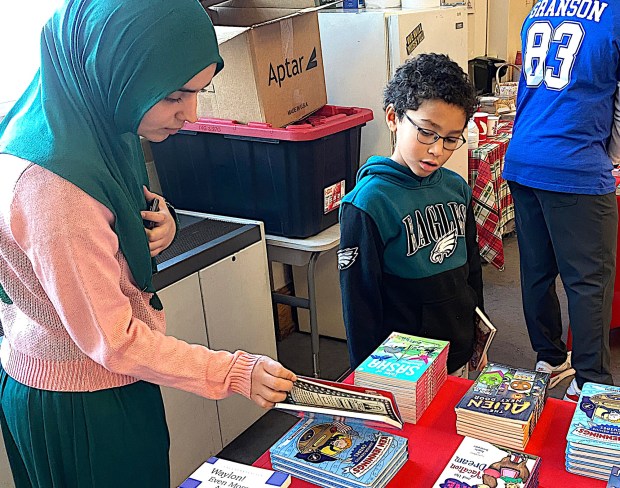 Garrettford Elementary substitute teacher Nimrah Khan helps third-grade student Jaxon Mixon pick a book during Kylen Granson's foundation's KG's Kids Karnival of Books. (PETE BANNAN-DAILY TIMES)