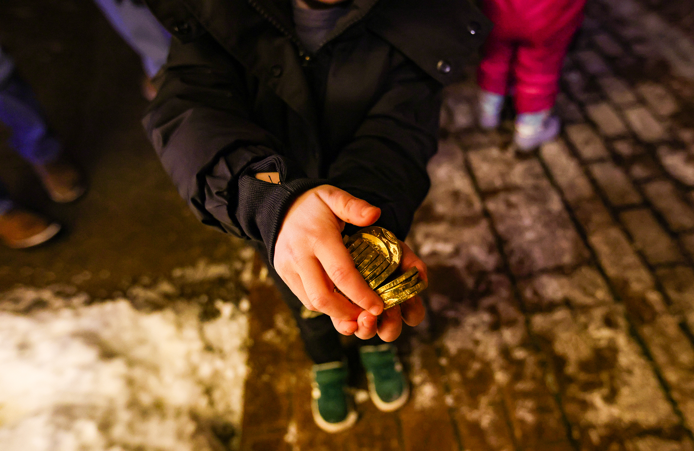 A kid holds out chocolate coins at the public menorah lighting Monday, Dec. 15, 2025, on Payrow Plaza outside Bethlehem City Hall.