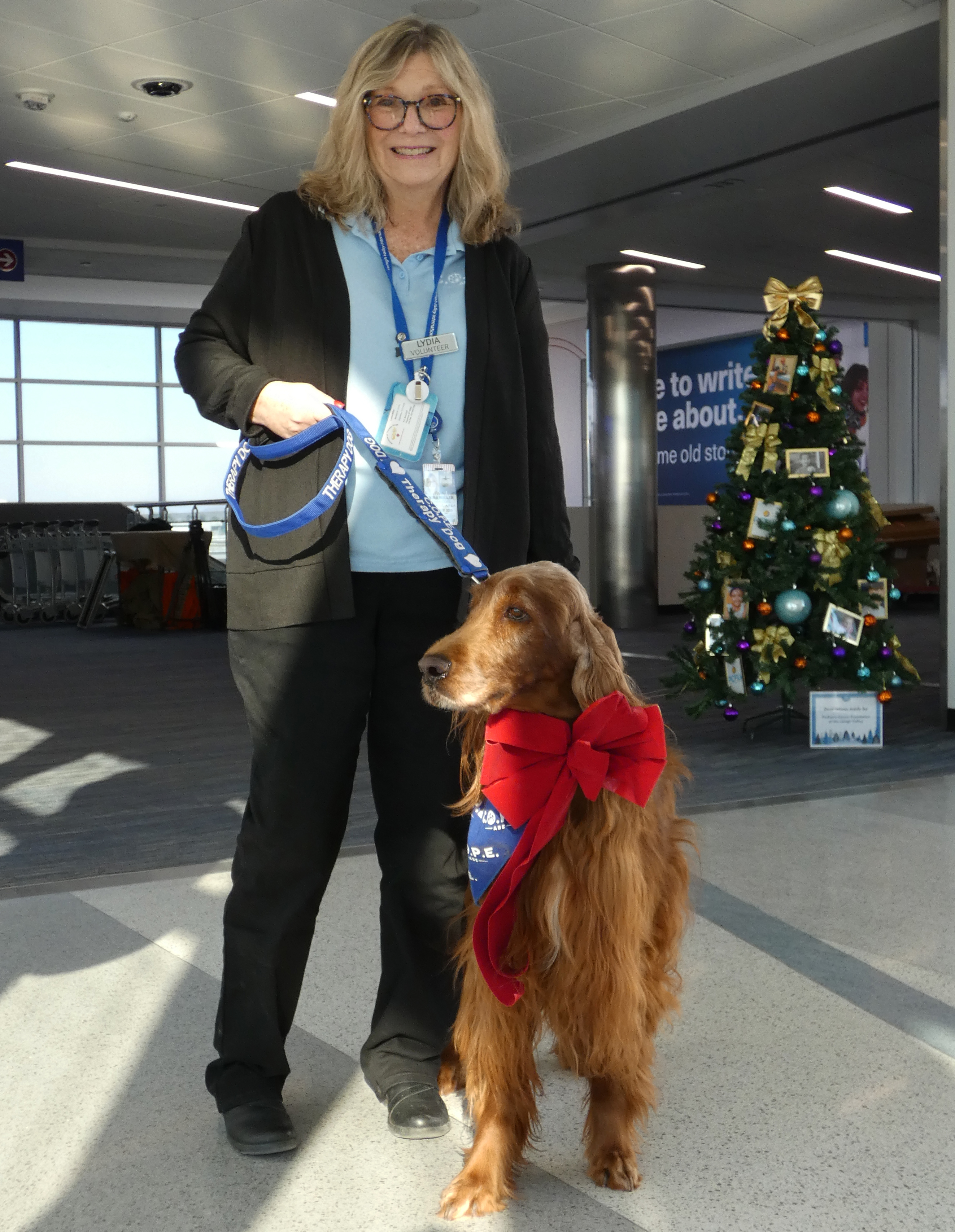 Lydia Miller with Harley, an Irish setter, join Lehigh Valley International Airport in marking 10 years of the Canines Offering Passengers Encouragement (C.O.P.E.) program Thursday, Dec. 18, 2025.