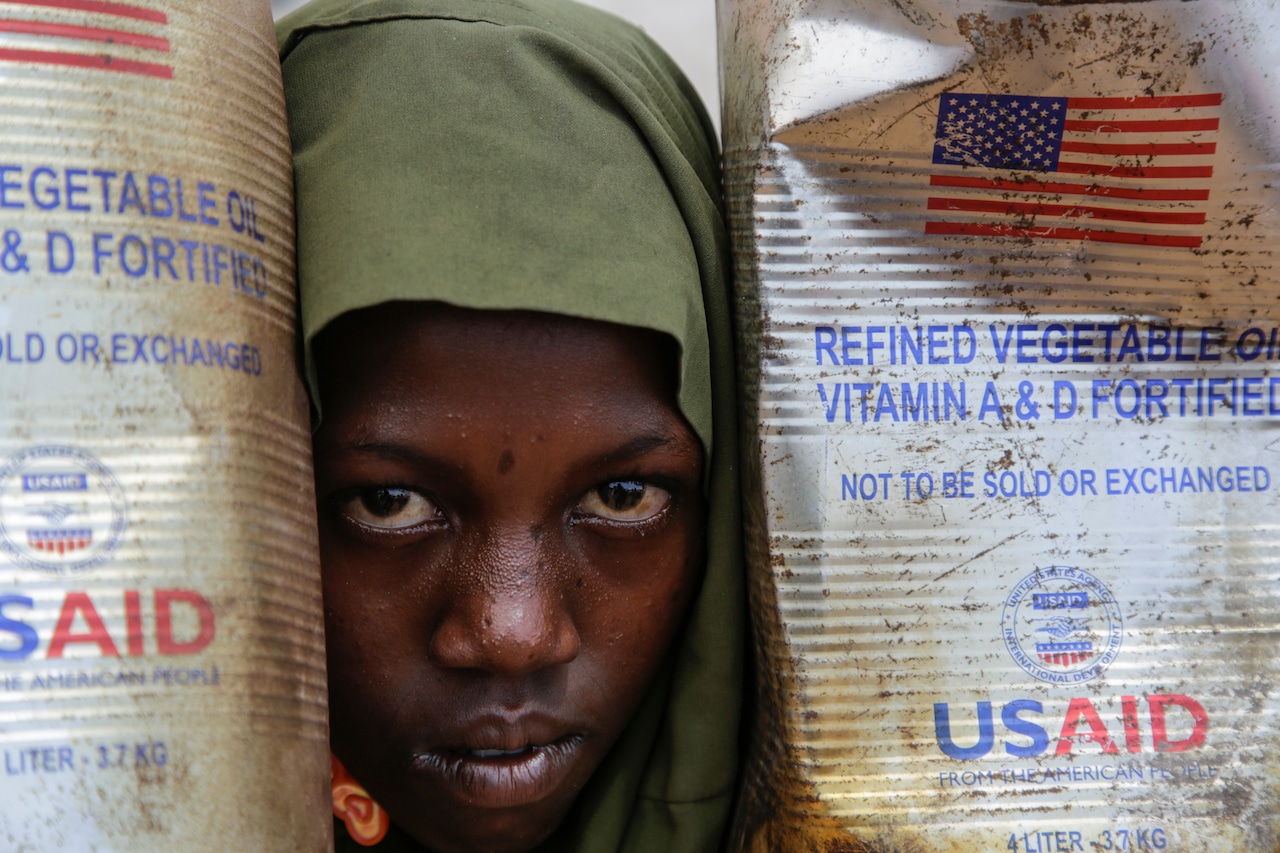 Somali child peers out from behind USAID oil containers.